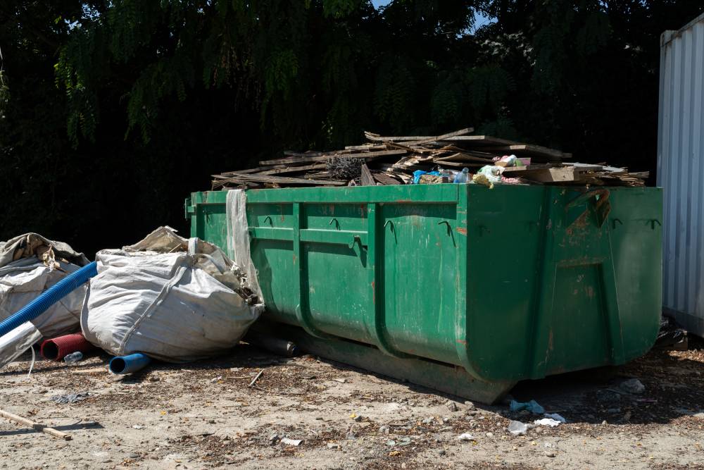 A green dumpster filled with a large pile of wooden debris, showcasing various sizes and shapes of wood materials